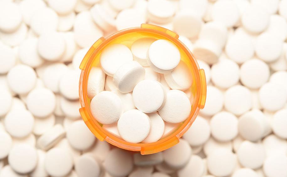 Opioid Crisis Concept: High angle view of a prescription bottled filled with pills surrounded by mor